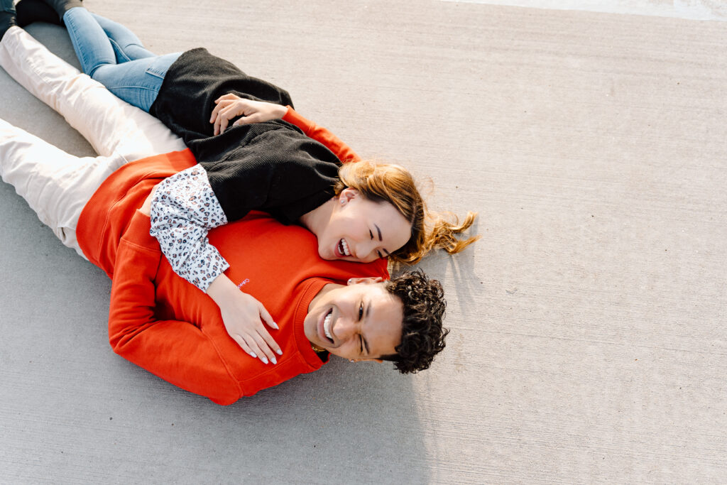 engaged couple laying on the cement ground in a cuddle position