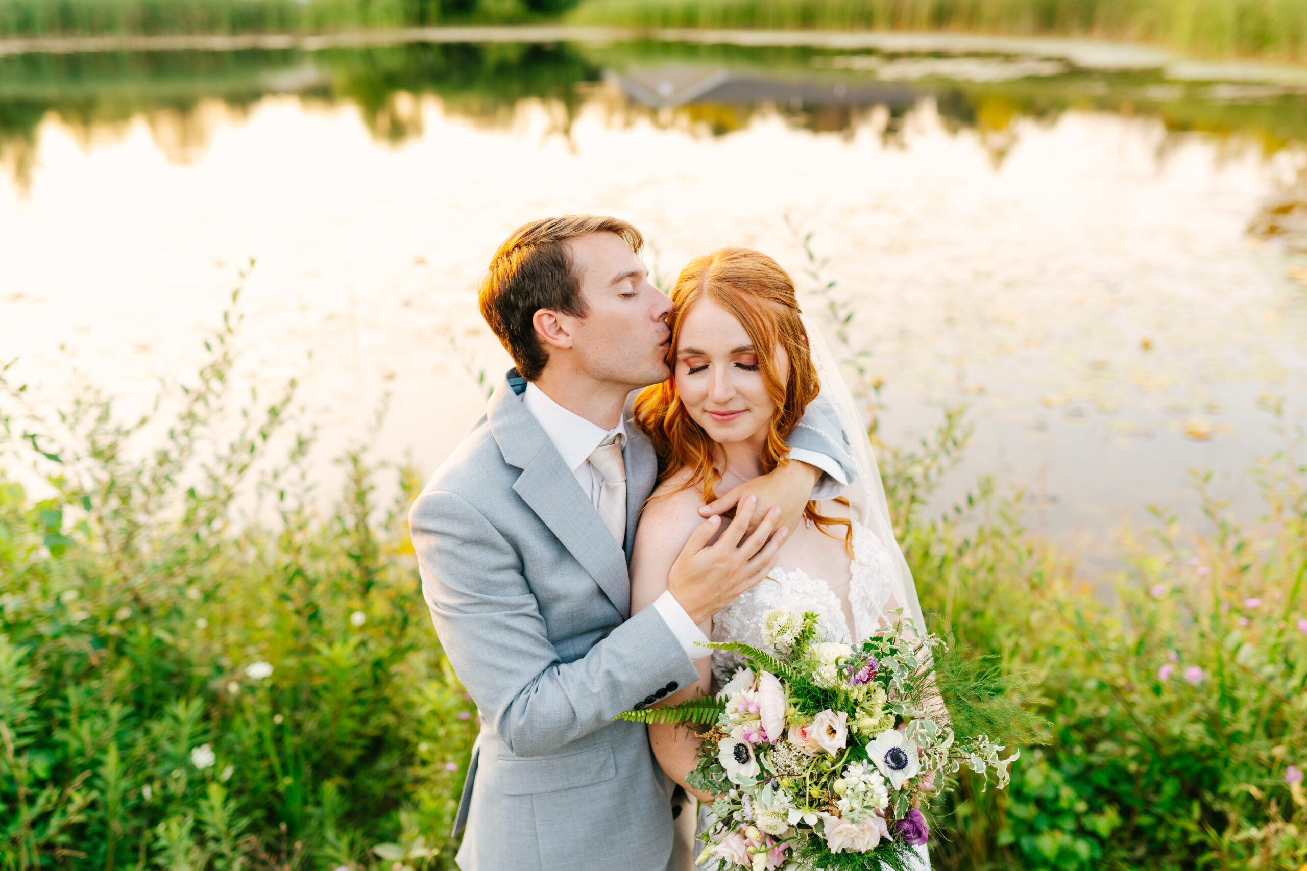 bride and groom embracing in front of pond during golden hour