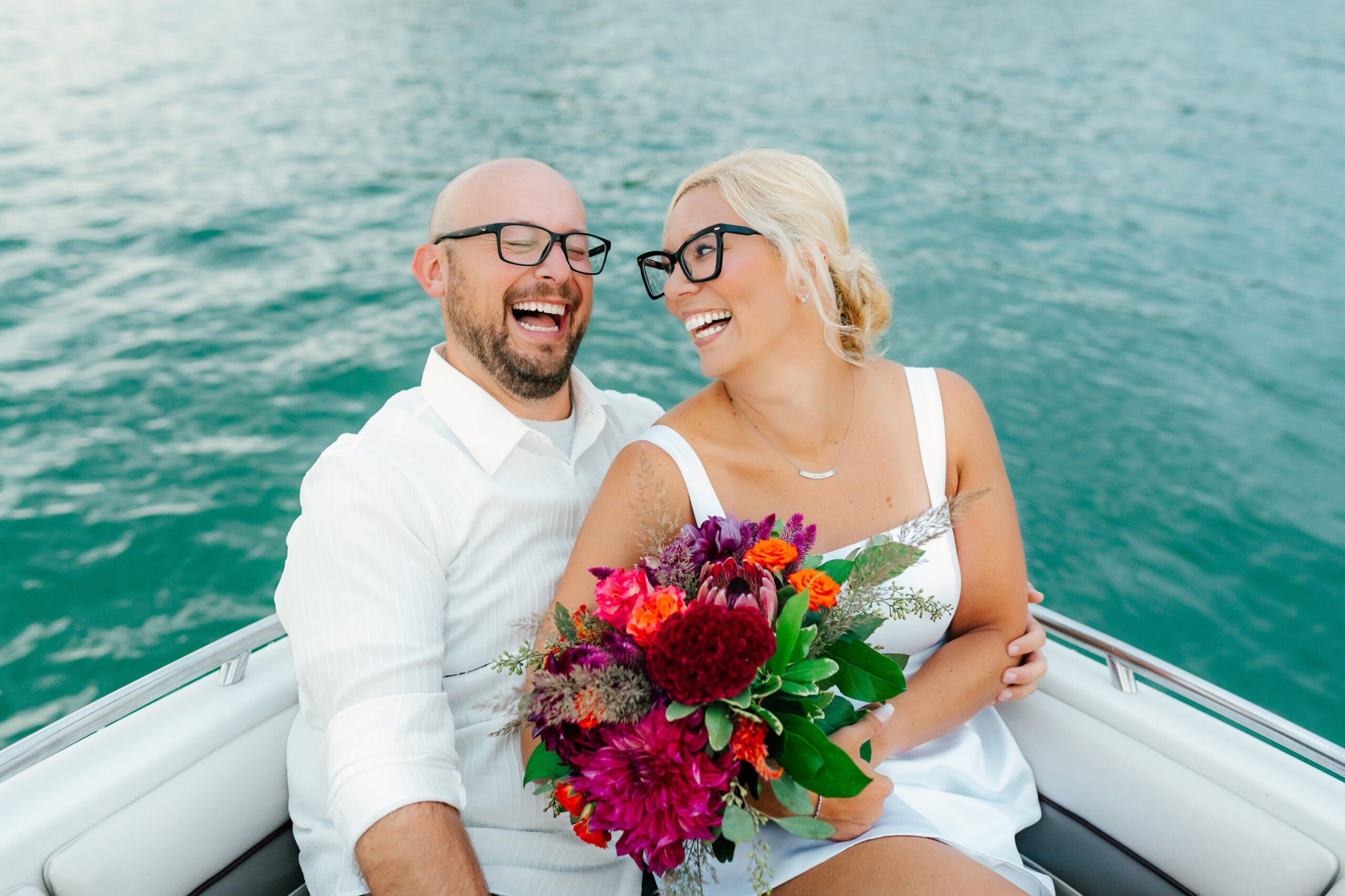 bride and groom laughing on a boat with colorful florals for a styled elopement