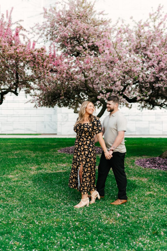 couple in front of the detroit institute of arts for engagement session walking hand in hand with spring blossoms in the background