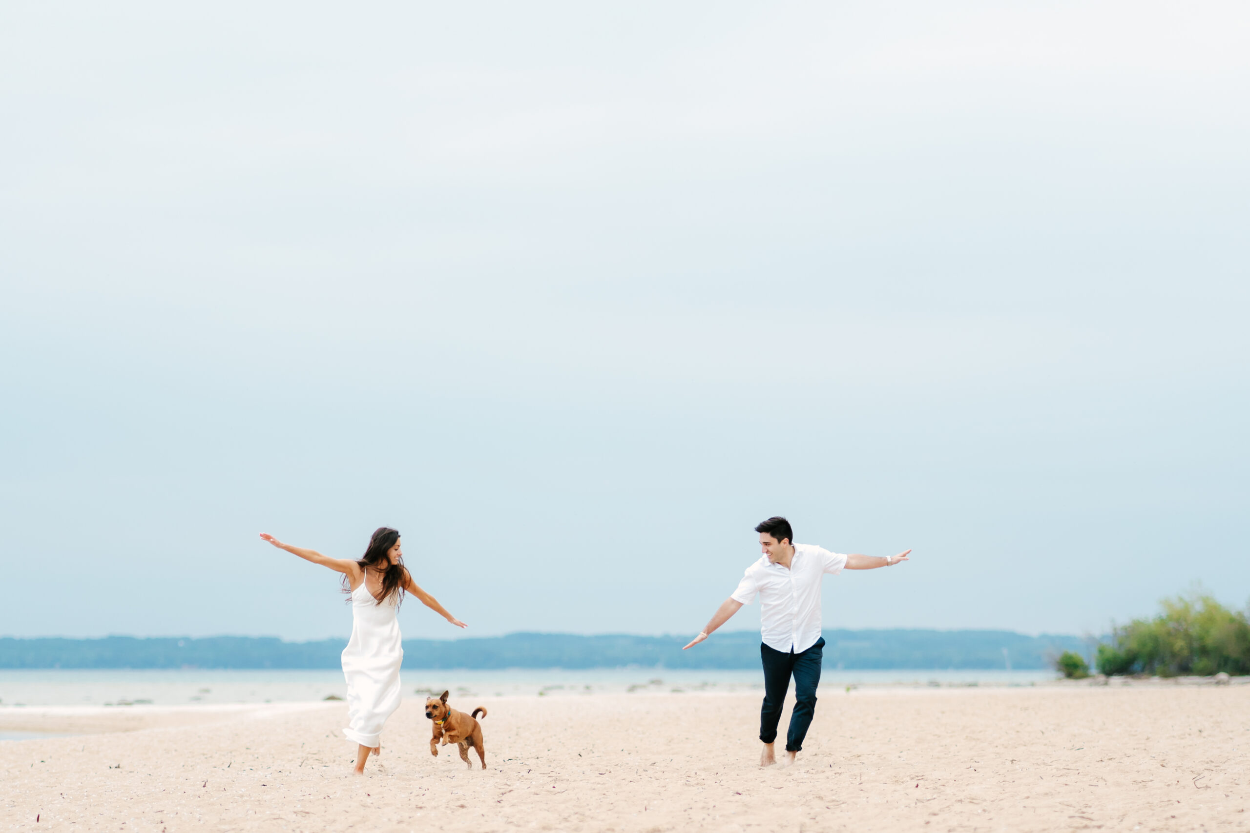 couple running on a michigan beach with their dog during sunrise for their engagement photos